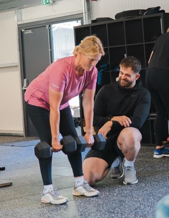 A woman performs squats alongside a man and another woman in a fitness setting, demonstrating teamwork and exercise.